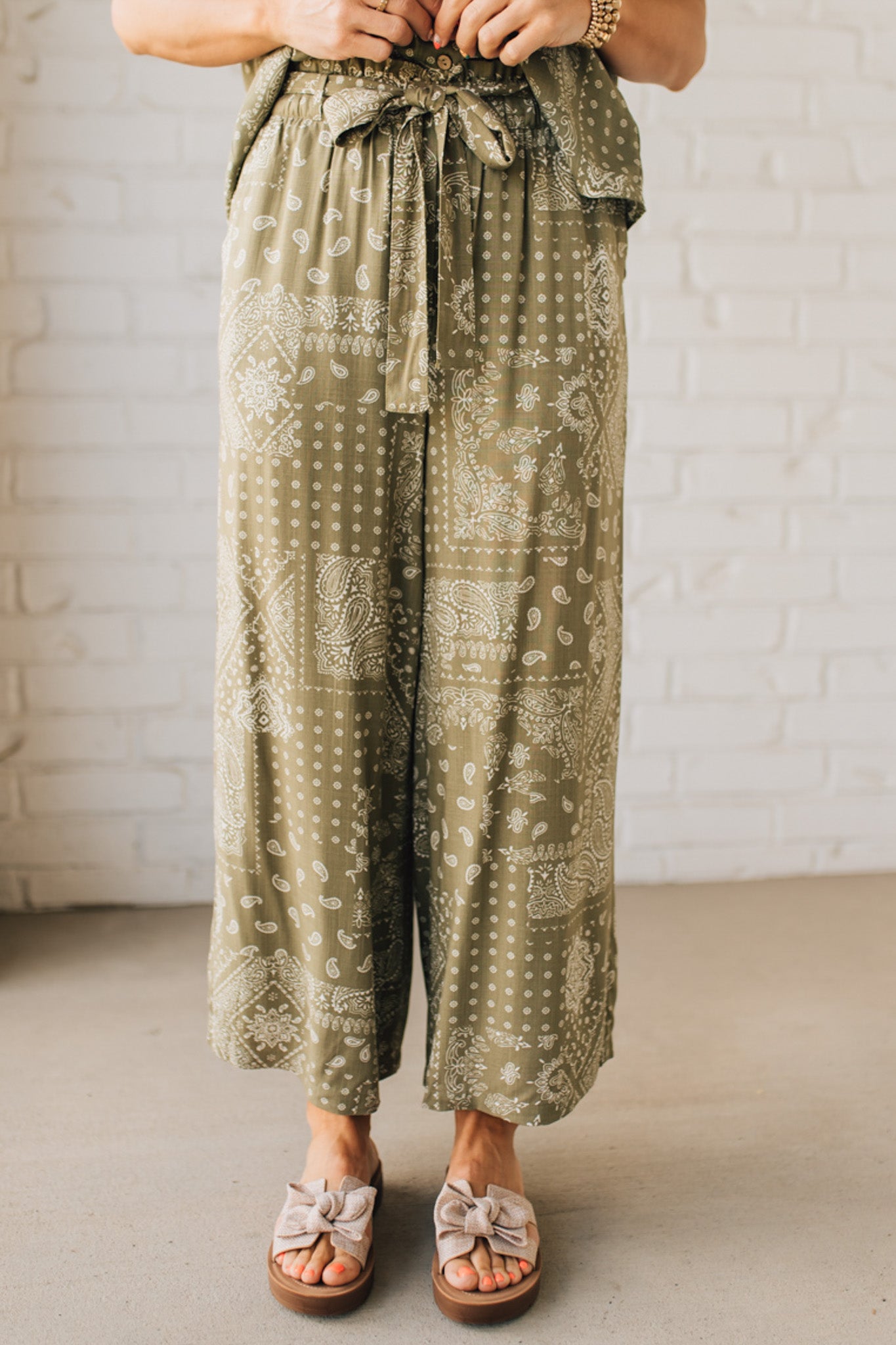 Blonde Woman in Tan Slides Wearing Paisley Print Belted Paper Bag Crop Pants.