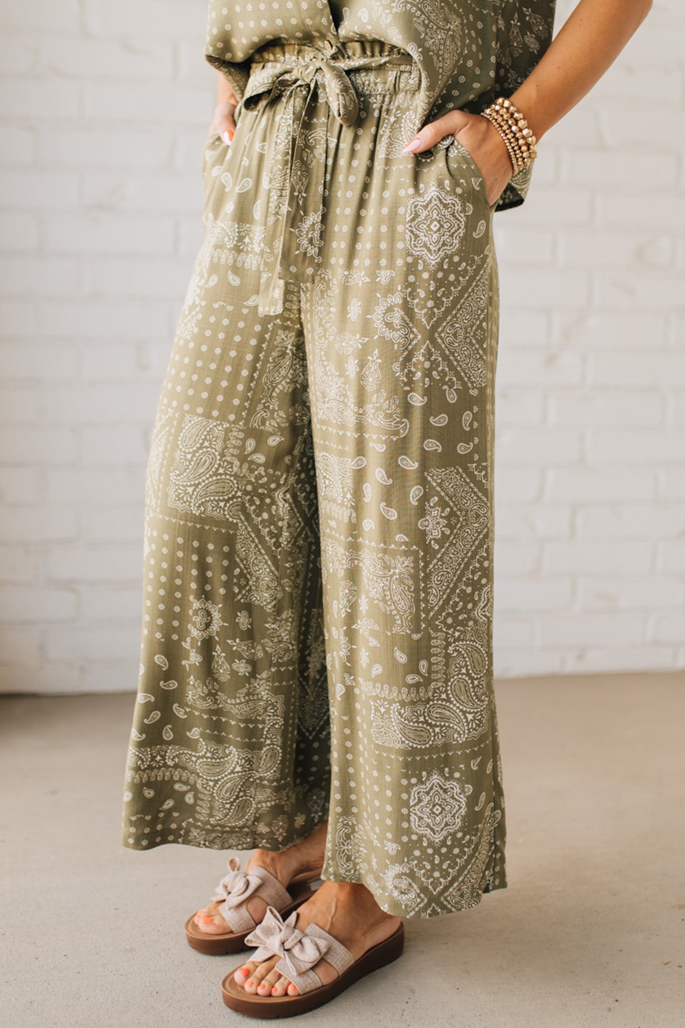 Blonde Woman in Tan Slides Wearing Paisley Print Belted Paper Bag Crop Pants.