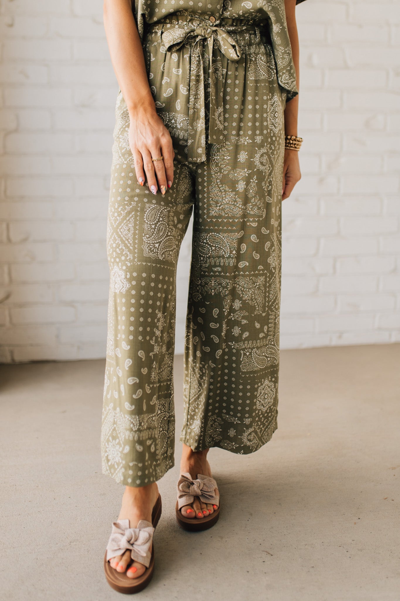 Blonde Woman in Tan Slides Wearing Paisley Print Belted Paper Bag Crop Pants.