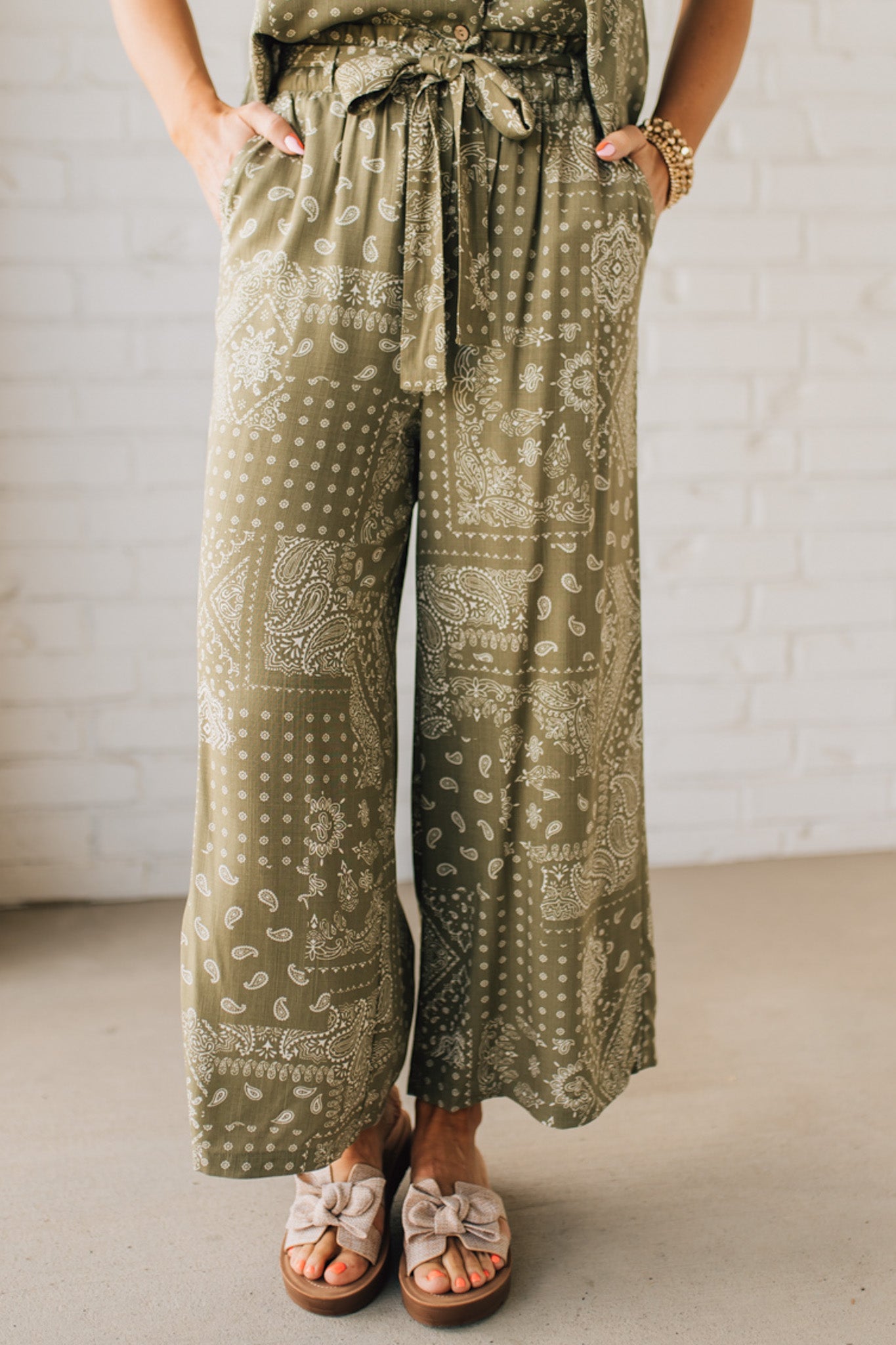 Blonde Woman in Tan Slides Wearing Paisley Print Belted Paper Bag Crop Pants.