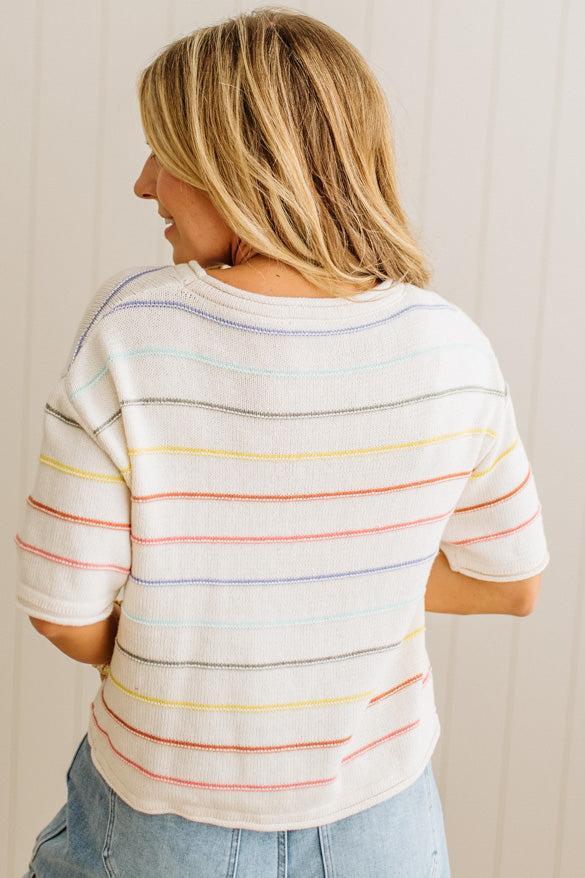 Woman wearing a white t-shirt with colorful horizontal stripes against a plain background