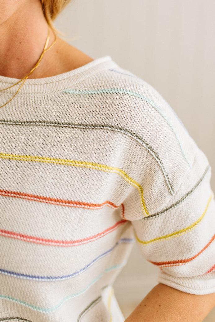 Close-up of a person wearing a white shirt with colorful stripes on a plain background
