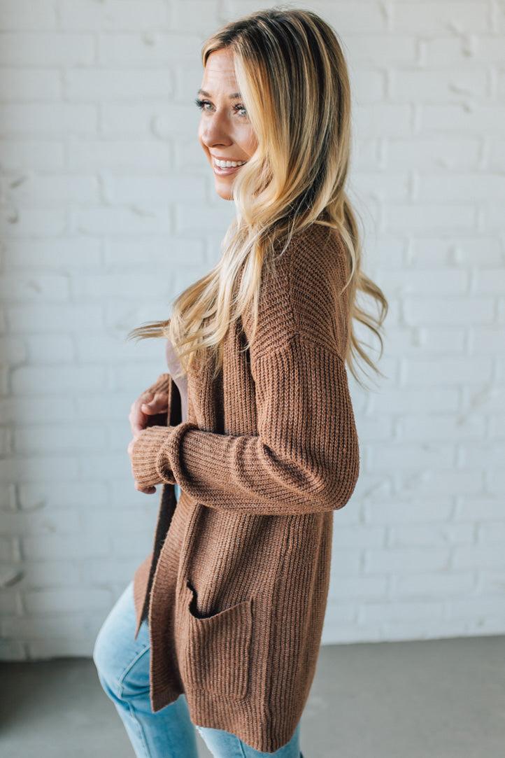 Woman wearing a brown cardigan in front of a white brick wall
