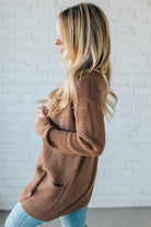 Woman wearing a brown cardigan against a white brick wall