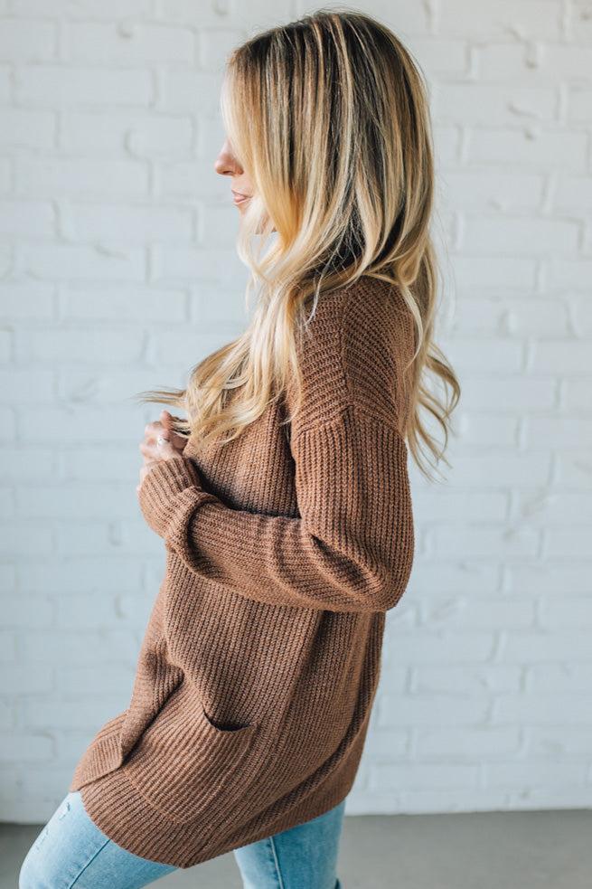 Woman wearing a brown cardigan against a white brick wall