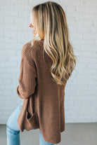 Woman wearing a brown cardigan against a white brick wall