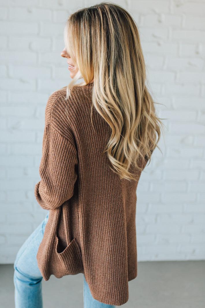 Woman wearing a brown cardigan against a white brick wall