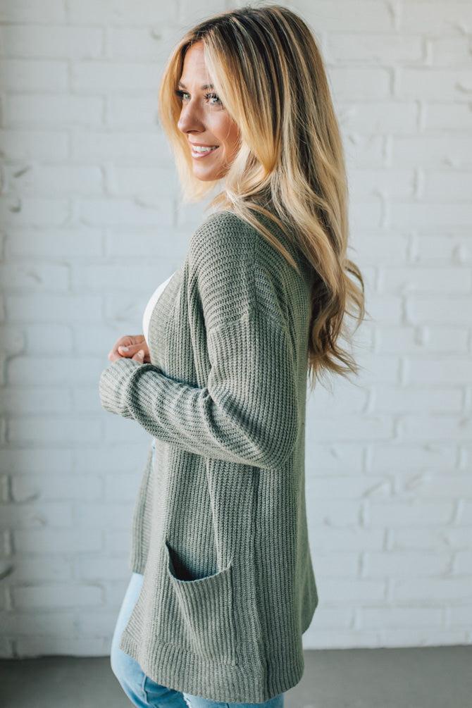 Woman wearing a green cardigan in front of a white brick wall