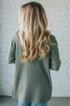 Person wearing a green knitted cardigan against a white brick wall.