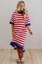 Woman wearing a red and white striped dress with blue trim against a white paneled wall.