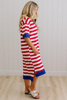 Woman wearing a red and white striped dress with blue trim against a white paneled wall.