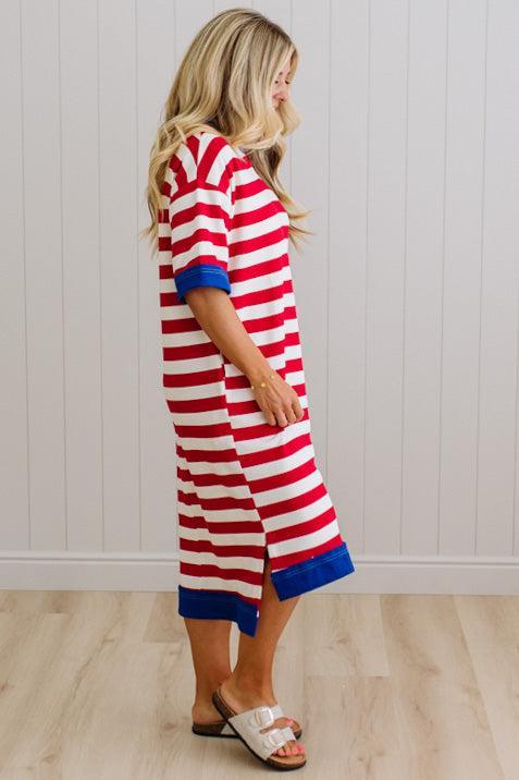 Woman wearing a red and white striped dress with blue trim against a white paneled wall.