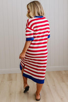 Woman wearing a red, white, and blue striped dress against a white paneled wall.