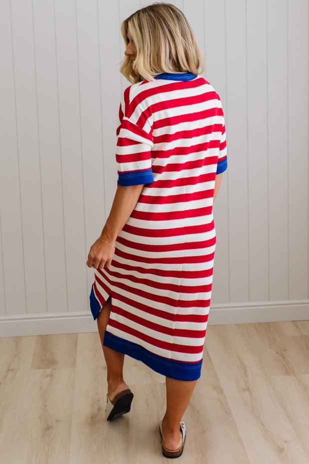Woman wearing a red, white, and blue striped dress against a white paneled wall.
