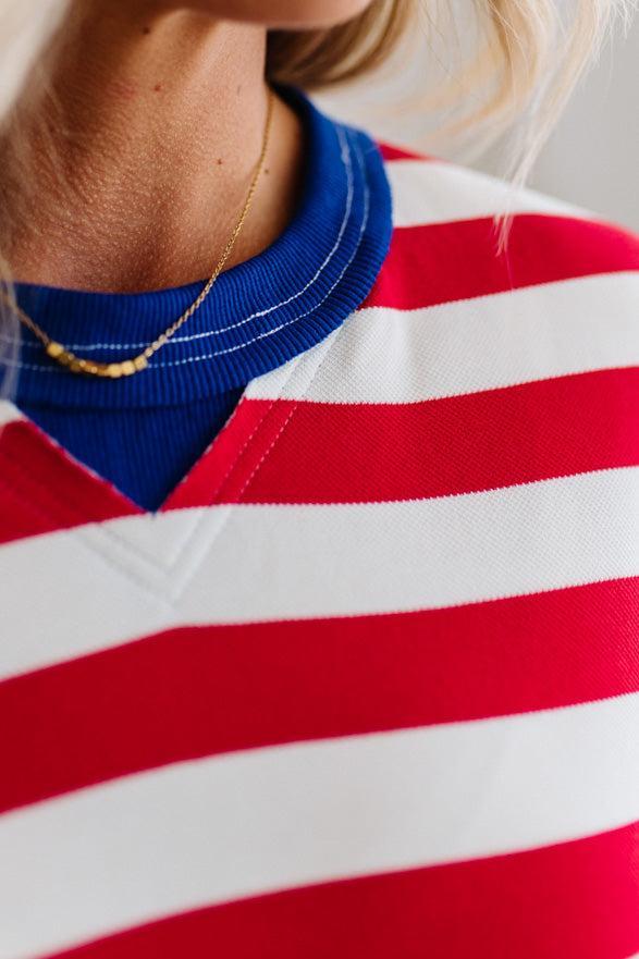 Woman wearing a red and white striped dress with blue trim against a white paneled wall.