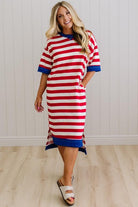 Woman wearing a red and white striped dress with blue accents against a white paneled wall.