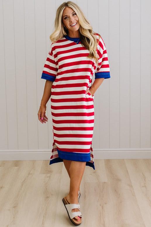 Woman wearing a red and white striped dress with blue accents against a white paneled wall.