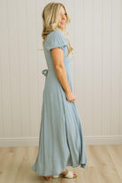 Woman wearing a light blue dress standing against a white paneled wall.