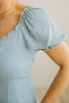 Light blue top with ruffled shoulders worn by a person, on a neutral background