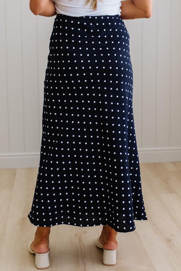 Person wearing a navy blue polka dot skirt with white background
