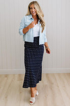 Woman wearing a light blue denim jacket, white top, and navy polka dot skirt indoors.