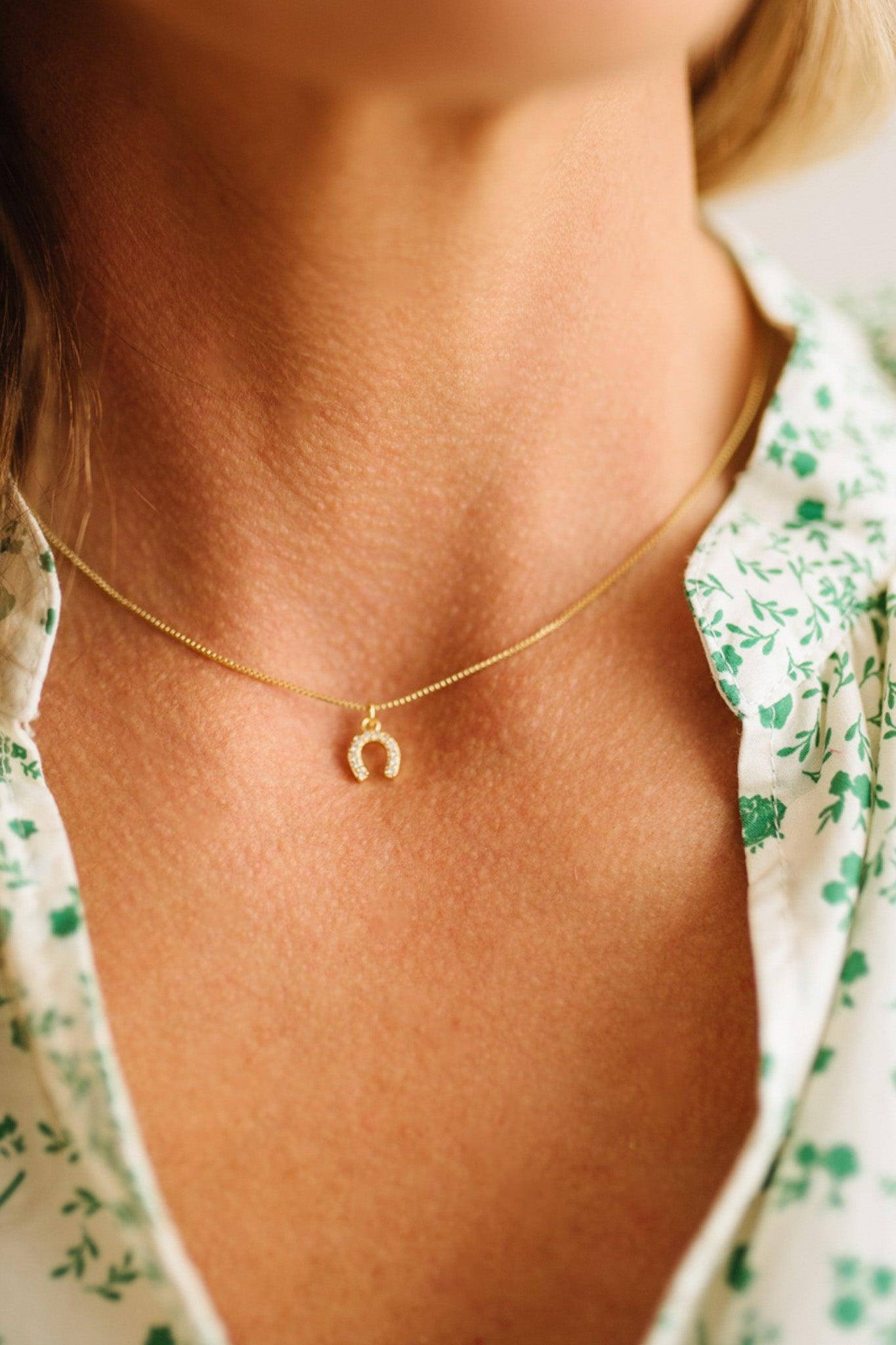 Gold necklace with a small pendant worn by a person with a floral shirt.