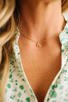 Close-up of a person wearing a delicate gold necklace with a small pendant, against a blurred background.