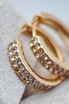 Gold hoop earrings with crystal embellishments on a light fabric background
