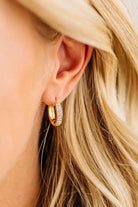 Close-up of a person wearing gold hoop earrings with small diamonds.