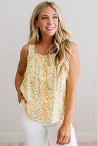 Woman wearing a floral sleeveless top and white pants against a light background