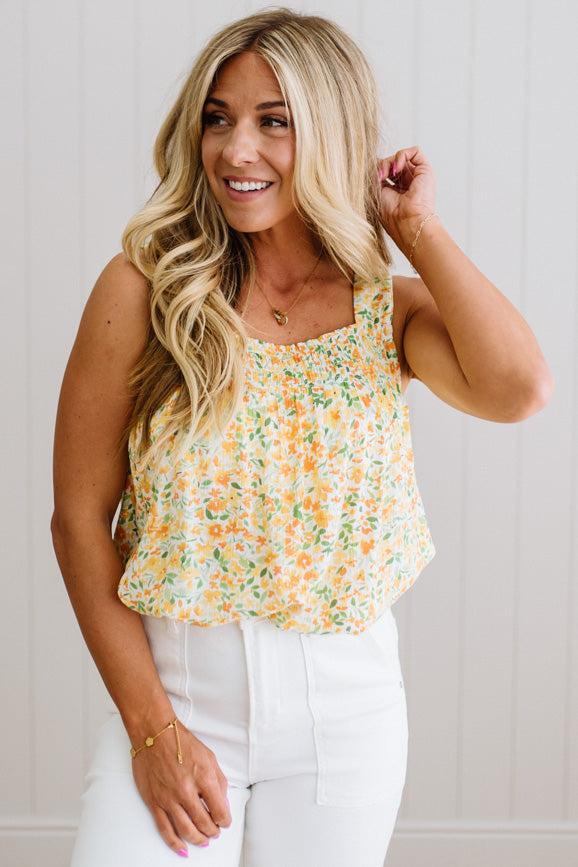 Woman wearing a floral tank top and white pants against a plain background
