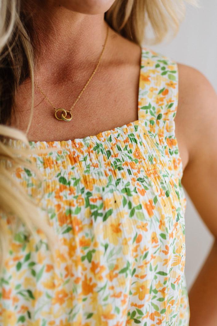 Woman wearing a floral top with a gold necklace featuring a double circle pendant.