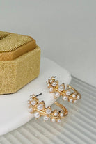 Gold earrings with pearl accents on a white surface next to a gold box.