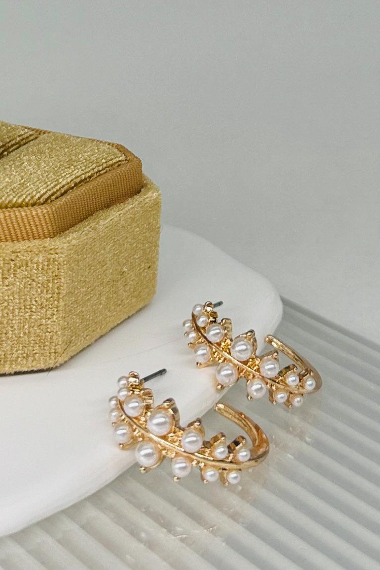 Gold earrings with pearl accents on a white surface next to a gold box.