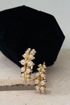 Gold and pearl earrings on a black cushion with a light background