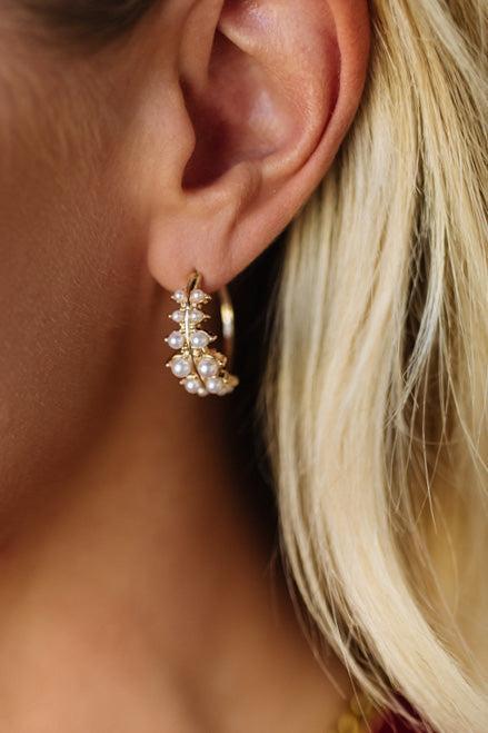 Close-up of an ear wearing a gold earring with pearl-like stones.