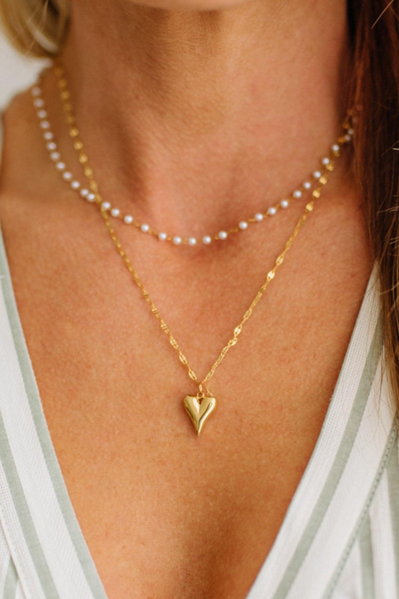 Gold heart pendant necklace on a person wearing a white and green striped top.