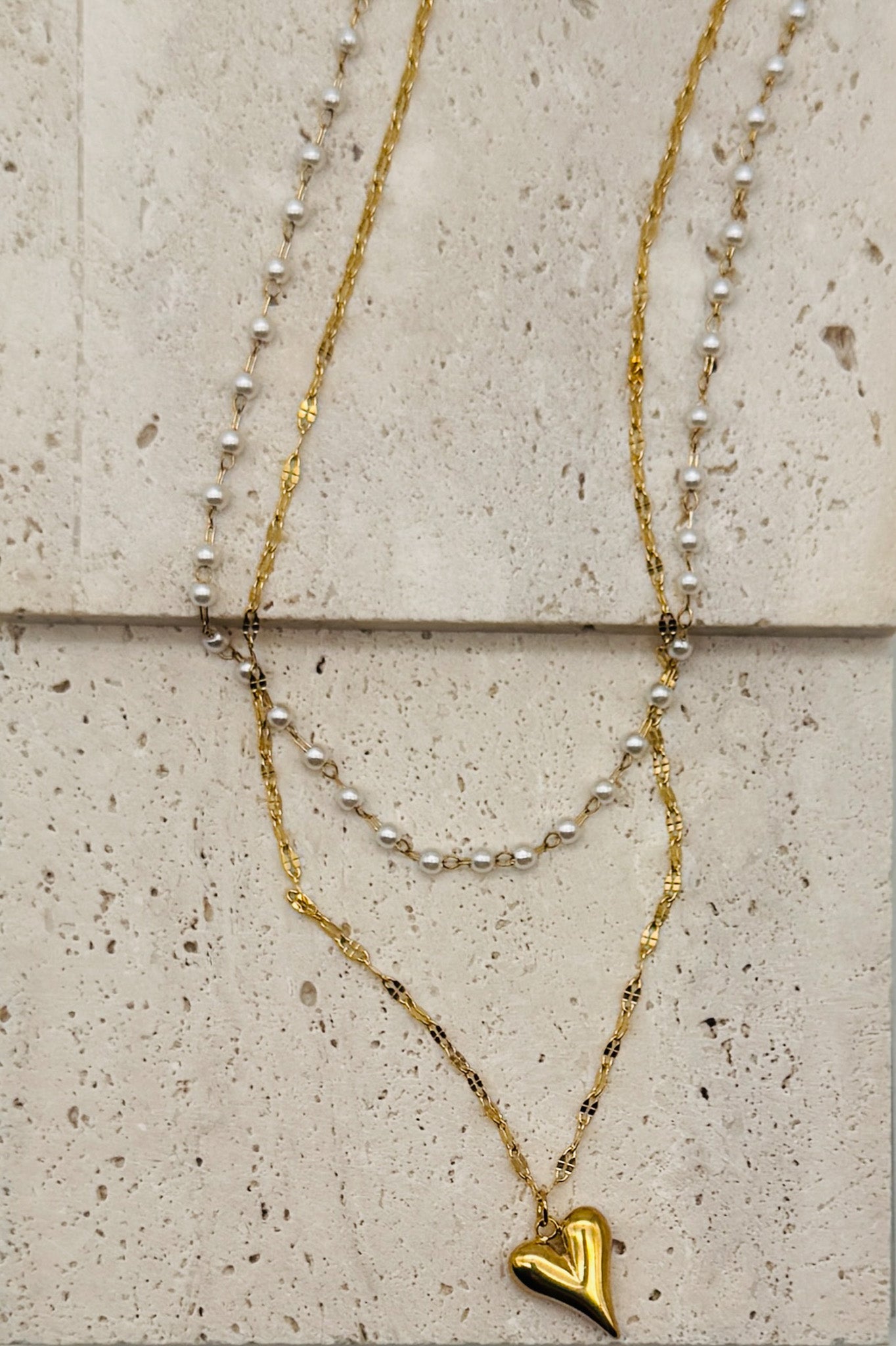 Two layered necklaces with heart pendants on a textured stone surface