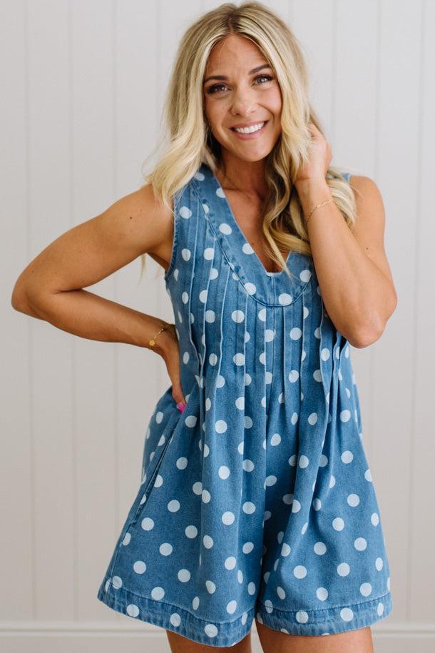 Woman wearing a blue polka dot romper against a white wall
