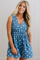 Woman wearing a blue polka dot romper against a white wall
