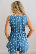 Person wearing a blue polka dot romper against a white paneled wall.