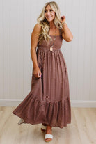 Woman wearing a brown polka dot dress standing against a white wall.