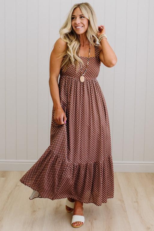 Woman wearing a brown polka dot dress standing against a white wall.