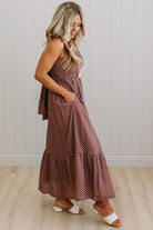 Woman wearing a brown polka dot dress standing against a white paneled wall.