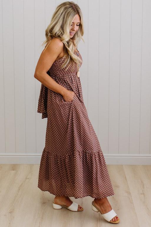 Woman wearing a brown polka dot dress standing against a white paneled wall.