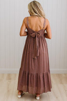 Woman wearing a brown polka dot dress with a bow detail, standing against a white wall.