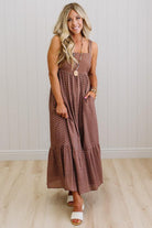 Woman wearing a long brown polka dot dress against a white wall.