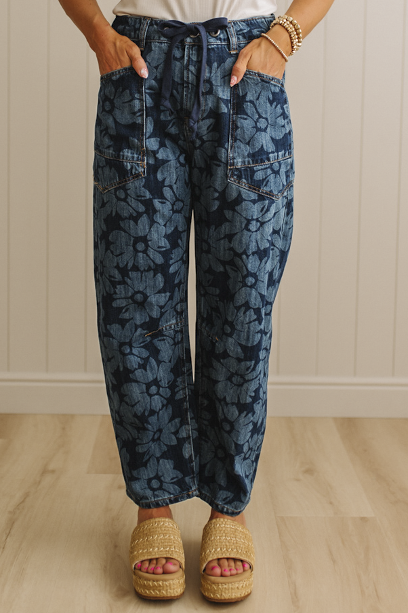 Person wearing blue floral-patterned jeans with a white wall background