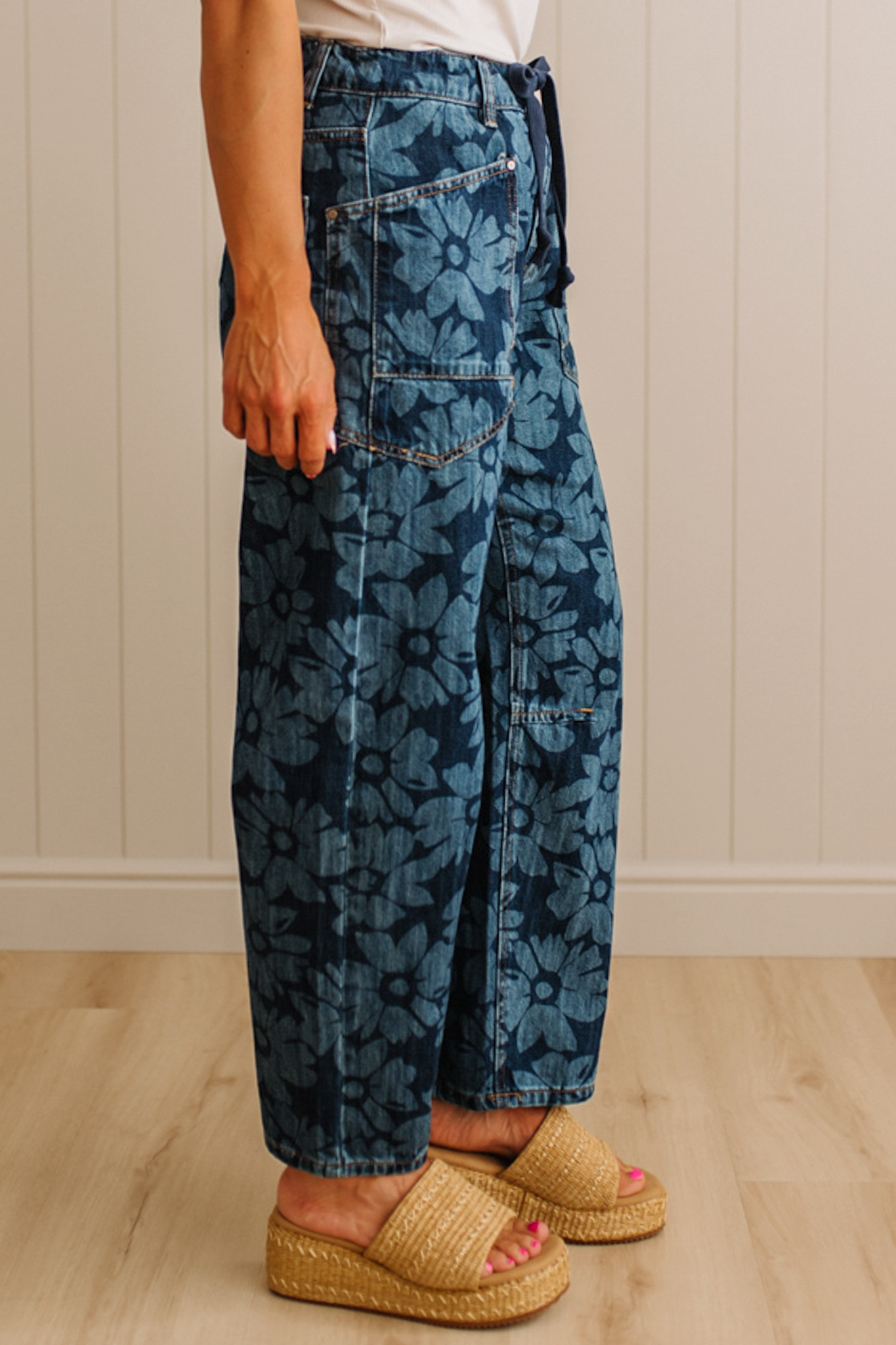 Person wearing blue floral-patterned pants standing on a wooden floor with a neutral wall background