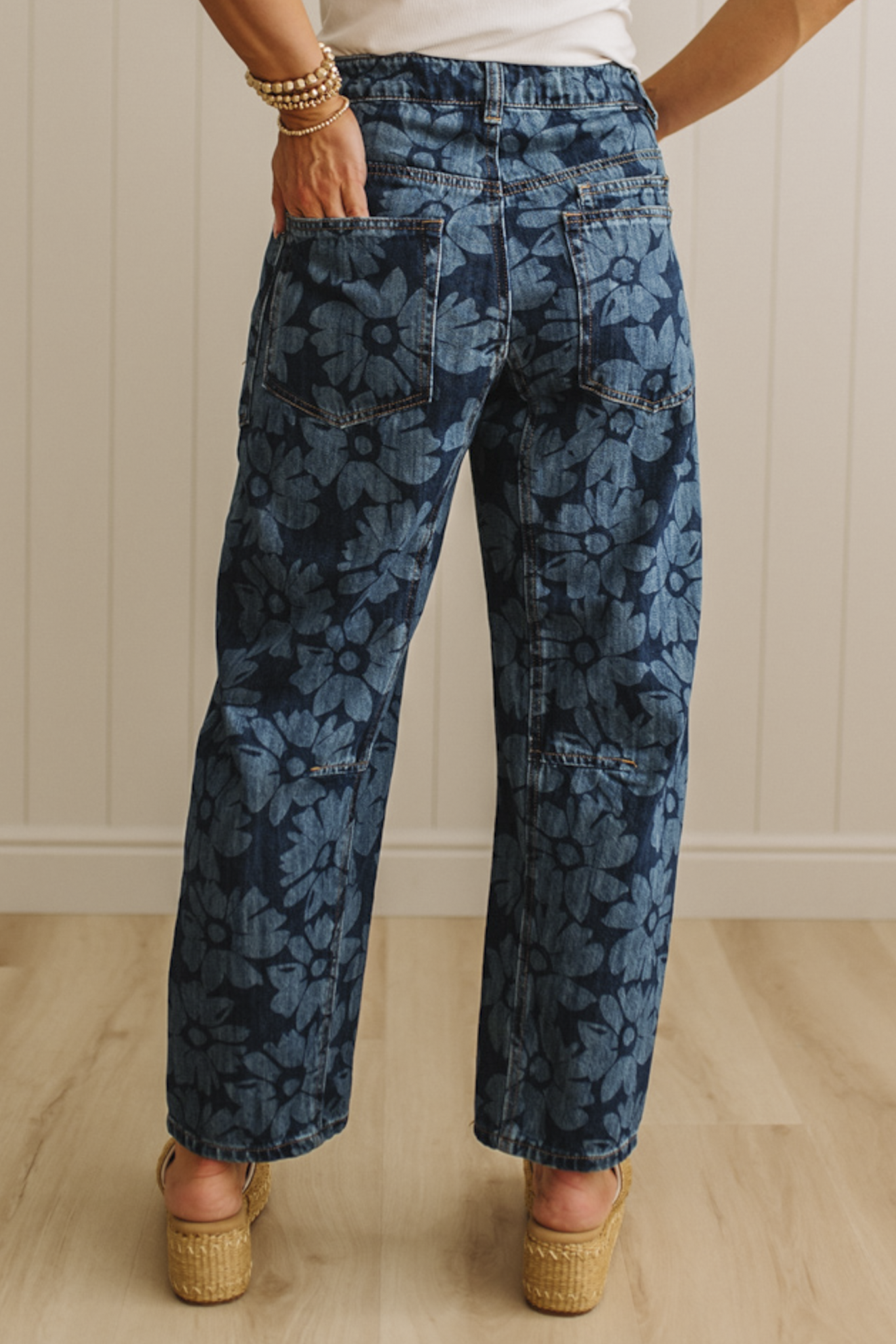 Person wearing blue floral-patterned jeans standing on a wooden floor.